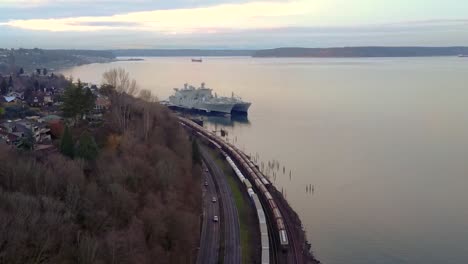 long train on the railroad by the bay in washington, usa with ships docked over the calm ocean near the shore on a sunset - aerial shot