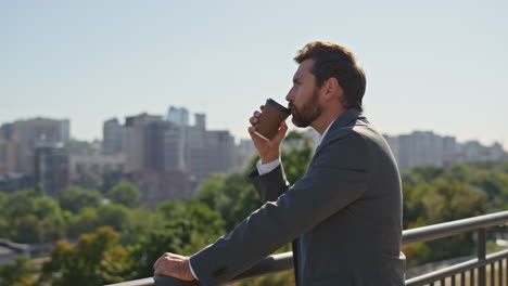 relaxed entrepreneur drinking coffee on street looking city panorama close up.