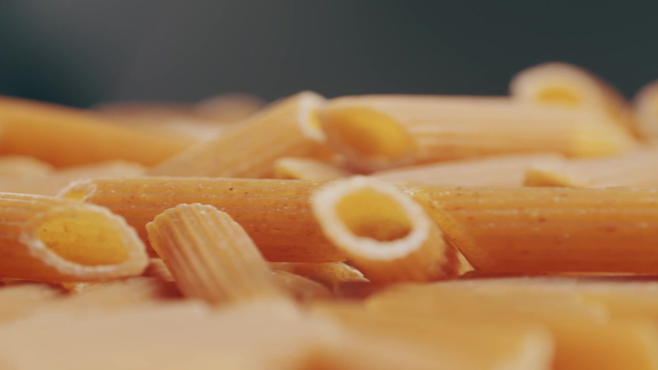 Pasta integrale biologica, maccheroni di semola di grano duro, penne rigate crude in una ciotola di legno. Filmato 4k di alta qualità