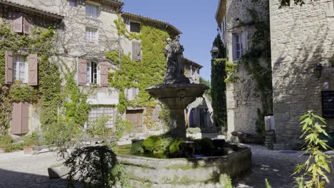 pintoresca pequeña plaza romántica con antiguas casas de piedra con hiedra y una pequeña fuente con una figura en el cálido sur de francia