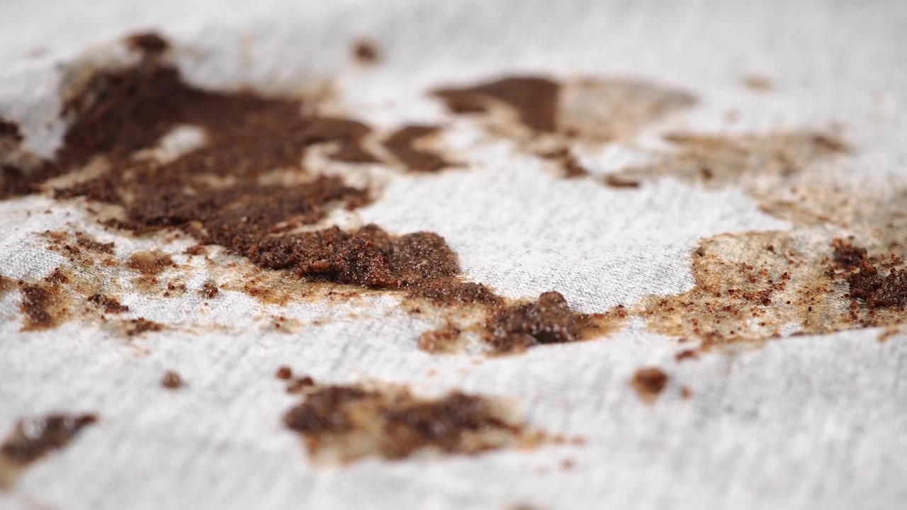 Nahaufnahme von Kaffeesatz und verschütteter Flüssigkeit auf weißem Stoff