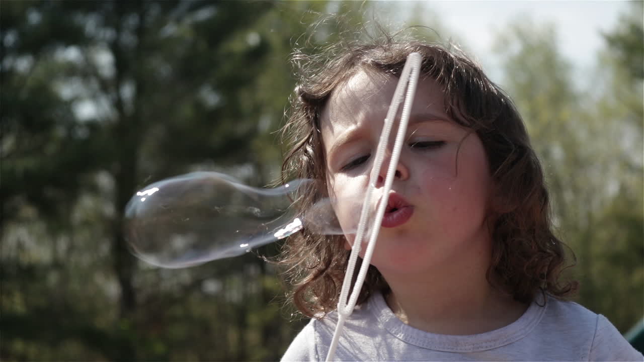 Young girl pulls out bubble wand and blows bubbles, slow motion close up