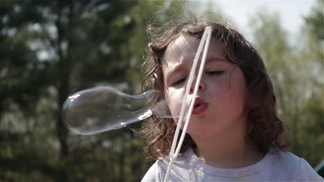 young girl pulls out bubble wand and blows bubbles, slow motion close up
