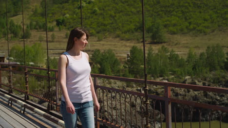 Woman-in-casual-clothes-walks-along-footbridge-against-hill