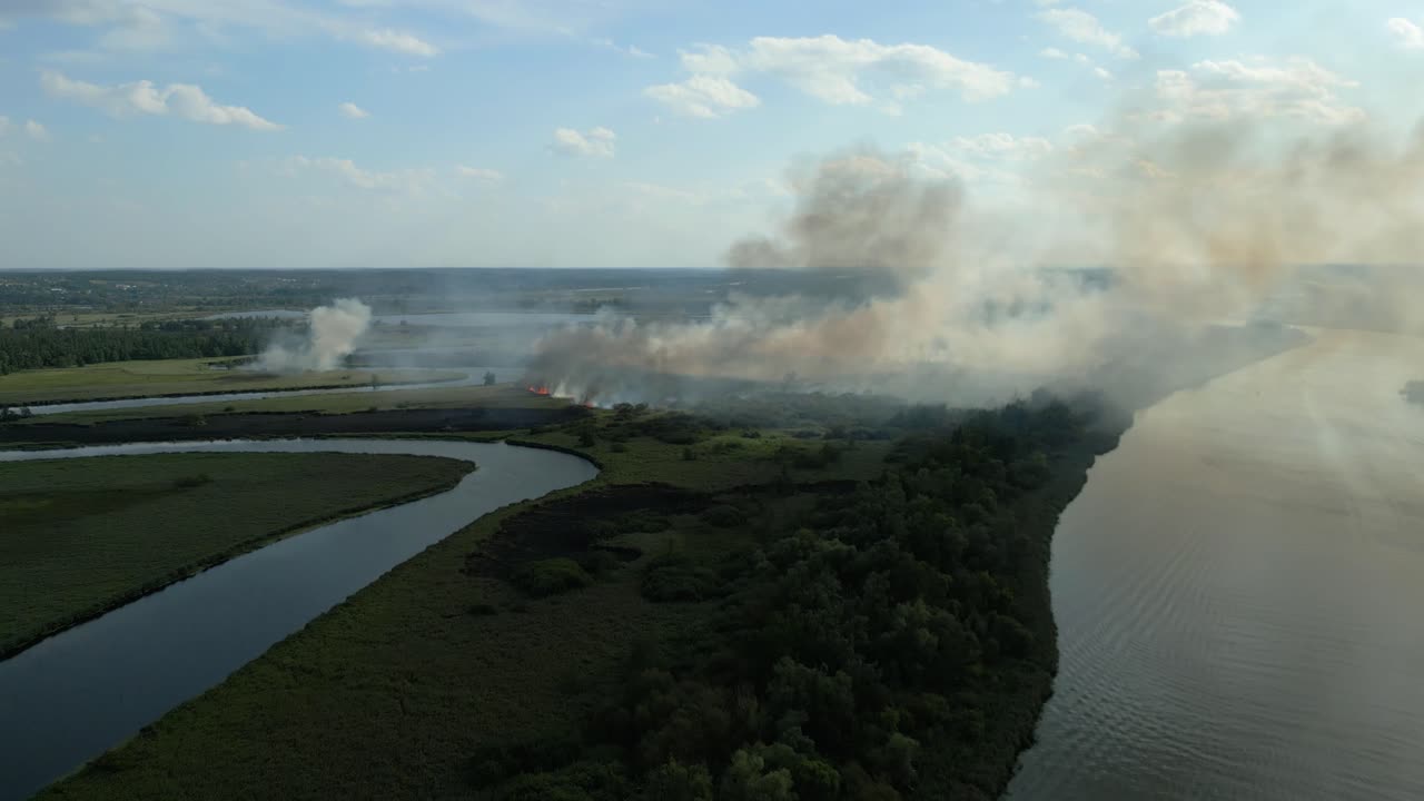 Wildfire spreads through grasslands near Odra River in Szczecin, Poland under a blue afternoon sky