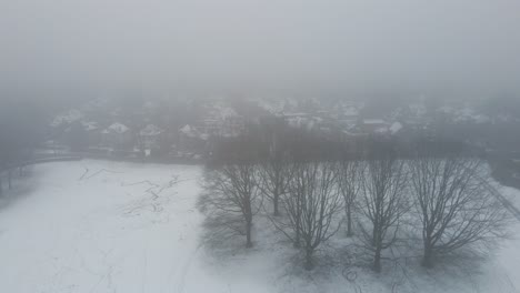 aerial of snow covered park at the edge of a suburban neighborhood in winter