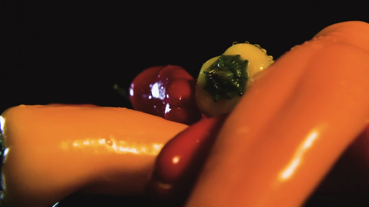 Slow spinning shot of fresh banana peppers in different colors covered with water drops and black background. Macro view. Commercial photography.