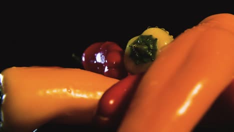 slow spinning shot of fresh banana peppers in different colors covered with water drops and black background. macro view. commercial photography.
