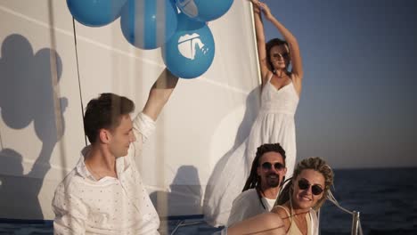 four friends having relaxing cruise on the yacht. they sitting on the ship board and enjoying the moment - guy waving the balloones, celebating. slow motion