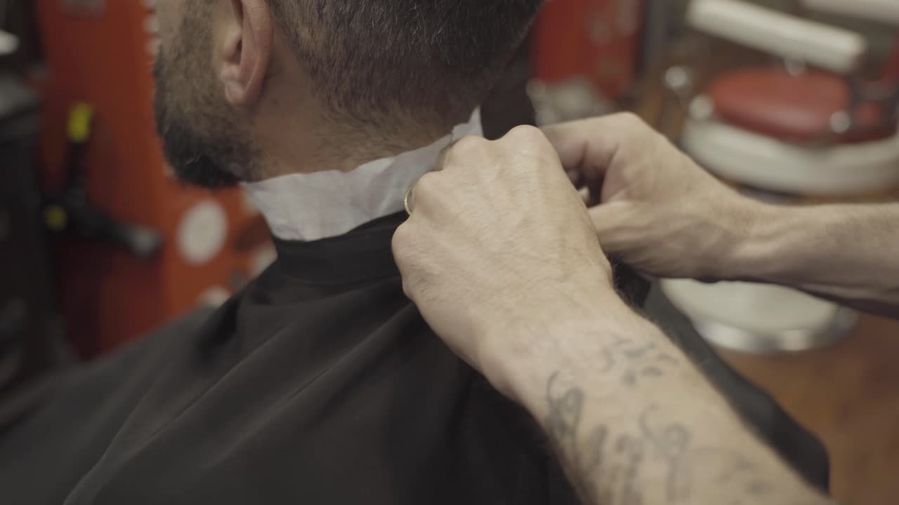 barbero poniendo una capa en su cliente en la barbería - de cerca