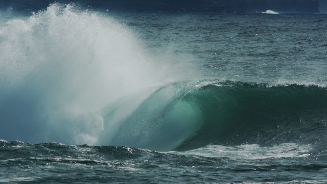 Huge curling wave crashes under bright sky as sea mist and spray explode outward, slow motion telephoto
