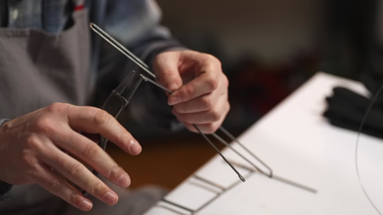 Primo piano di un artigiano che usa le pinze per piegare il filo d'acciaio in un laboratorio tradizionale slovacco di lavorazione del filo. Processo artistico in metallo fatto a mano Drotarstvo e concetto di abile maestria artigianale.