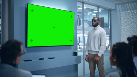 office conference room meeting presentation: charismatic black businessman talks, uses green screen chroma key wall tv. successfully presenting a e-commerce product to group of multi-ethnic investors