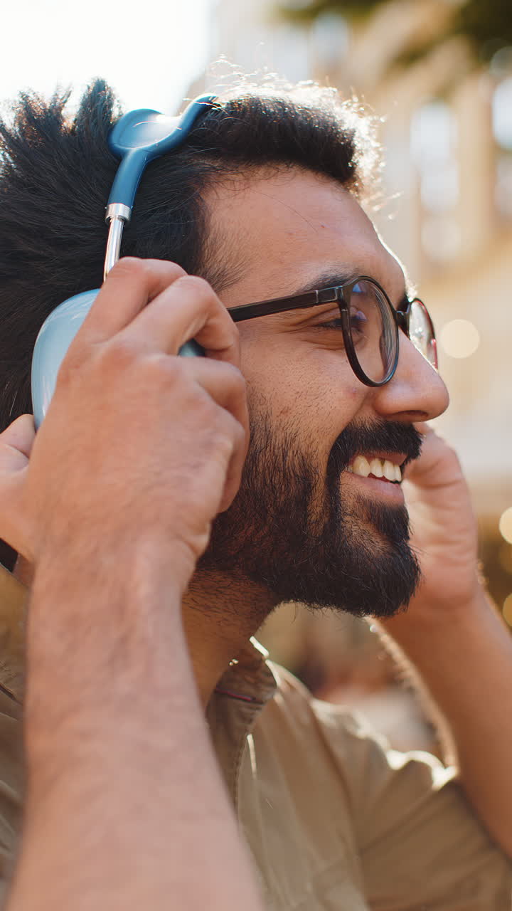 Happy young man in wireless headphones choosing listening music dancing outdoors city street