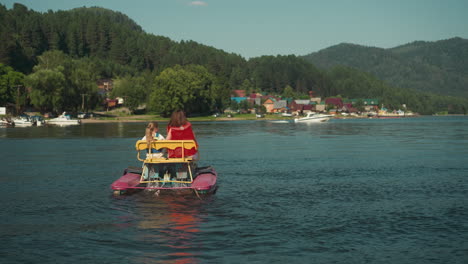 ein paar schwestern sitzt in einem katamaran auf dem fluss und schaut auf ein schnellboot. aktiver zeitvertreib am wochenende in langsamer bewegung. touristen haben spaß auf dem wasserverkehr.