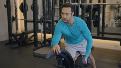 un hombre en camisa azul está haciendo un brazo dumbbell ejercicio de fila, trabajando la mayoría de los músculos de la espalda