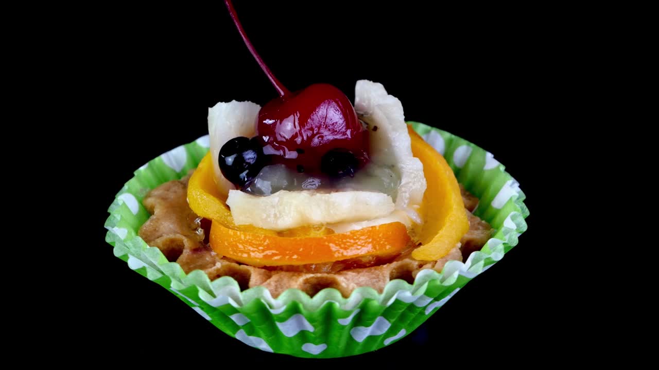 크림 컵케이크와 체리, 베리, 검은 바탕의 과일은 천천히 회전합니다.