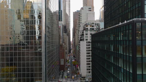 Forwards-fly-above-street-in-city.-Road-lined-by-tall-office-or-apartment-buildings.-Glossy-glass-facade-reflecting-surroundings.-Manhattan,-New-York-City,-USA