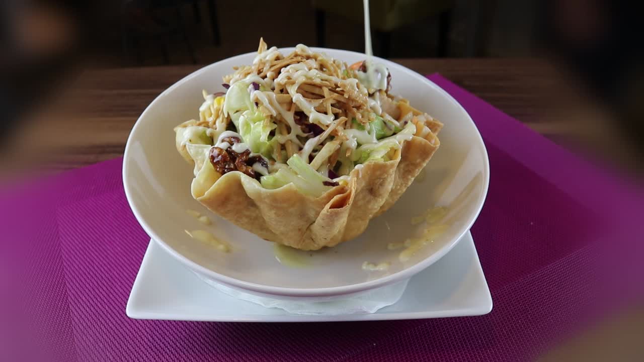 Versando il condimento su un'insalata taco fresca in una ciotola di tortilla croccante