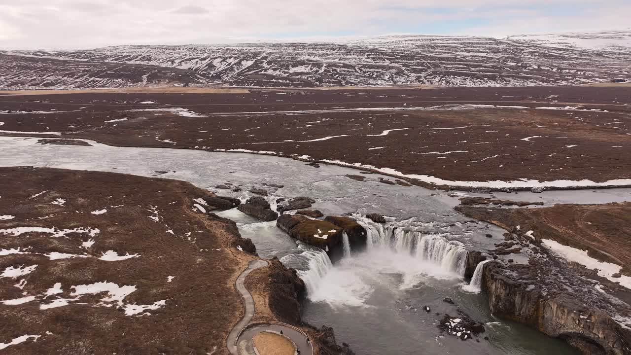 Aerial view of Goðafoss waterfall in late winter, cascading from the Skjálfandafljót river near Laugar, Iceland. Rugged snowy landscape surrounds the "Waterfall of the Gods".