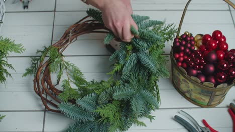 making rustic christmas wreath. hands holding green branches on rustic wooden background. seasonal holiday workshop online, making festive decorations at home