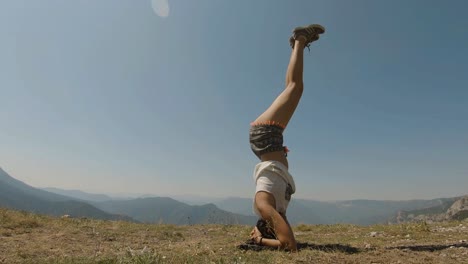 una joven haciendo un headstand recto en la cima de una montaña