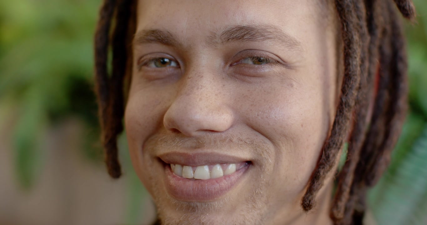 African American man holding gaze with camera, smiling gradually at home showing dreadlocks