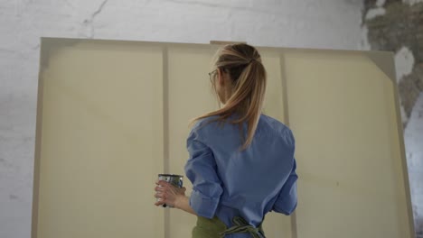 woman taking large paintbrush standing in front wide canvas