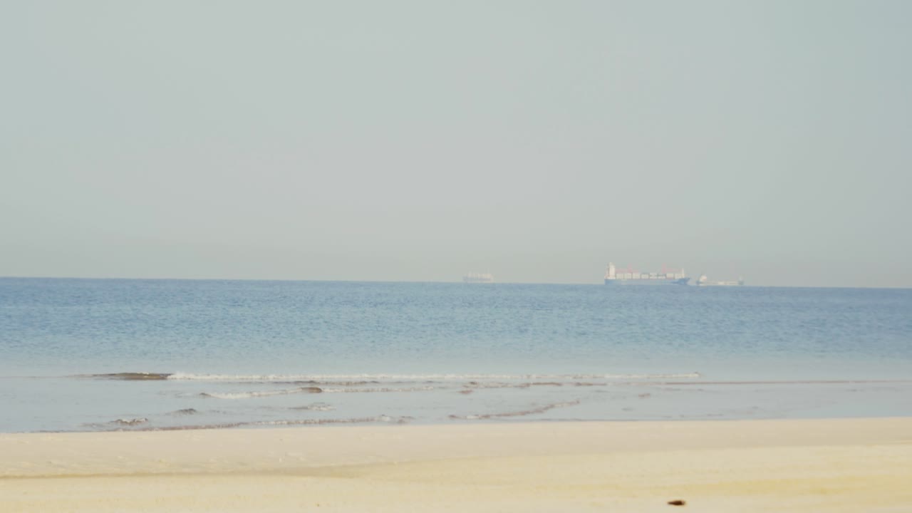 Cargo Ship on Calm Sea Viewed from Sandy Beach – Maritime and Coastal Scene