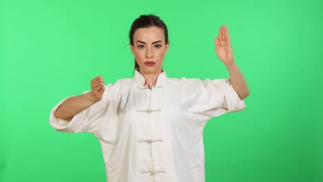 Beautiful-brunette-young-woman-in-white-kung-fu-wushu-uniform-practicing-martial-arts-while-looking-in-camera