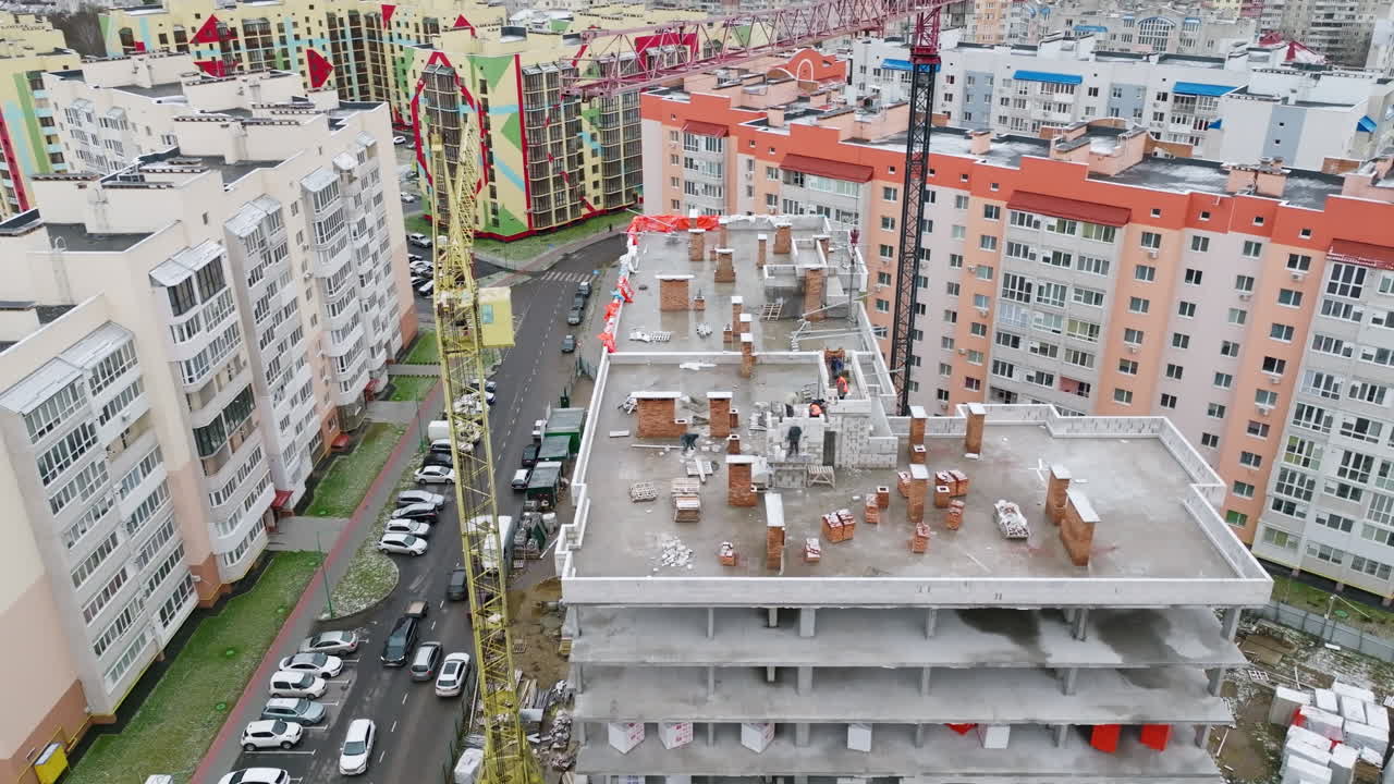New block of flats being constructed in the area. Slow approach to the construction site on the roof of the building with people working at it.