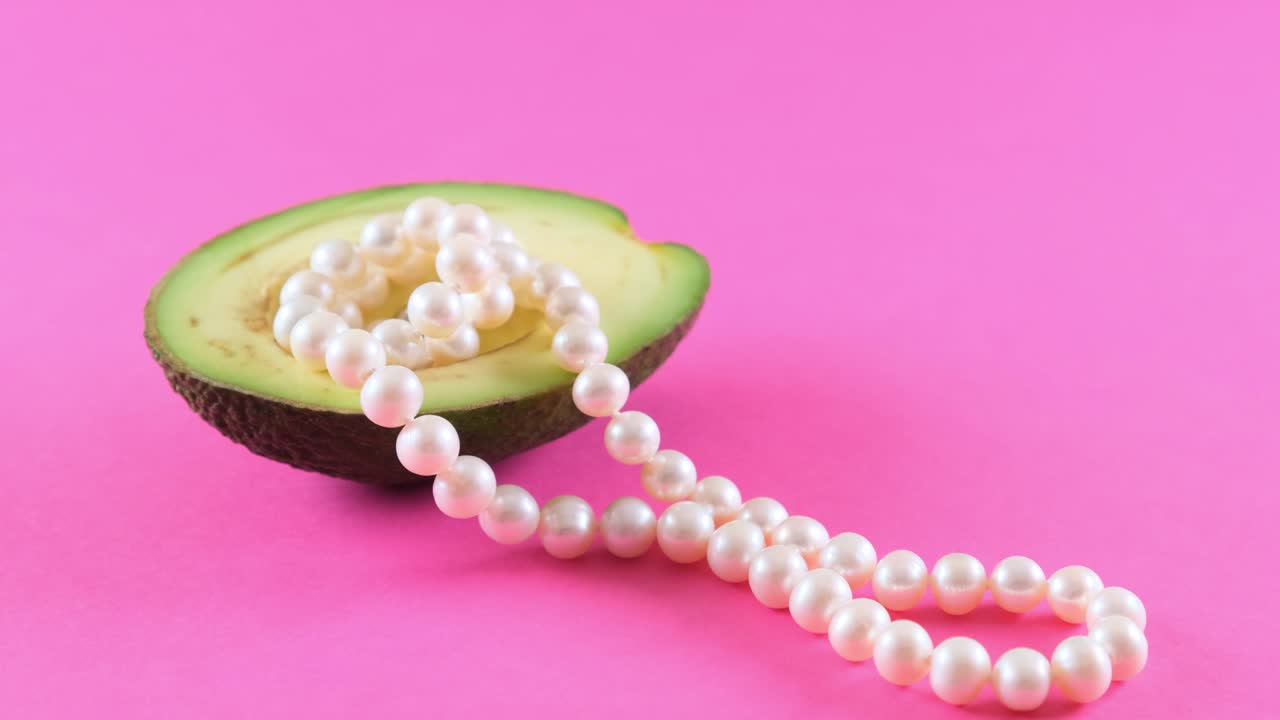 medio fruto de aguacate fresco con perlas en un fondo rosado. diseño de alimentos de moda