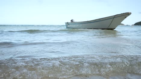 low angle view of an empty boat moored in shallow waters with gentle waves breaking on the shore, conveying a sense of tranquility and calm