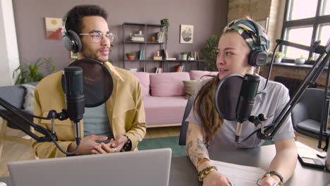 front view of young african american man and caucasian woman wearing headphones sitting at a table with microphones while they recording a podcast