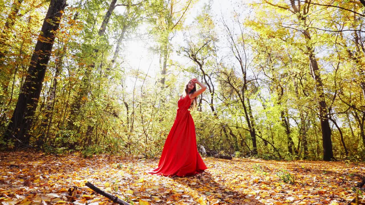 A Beautiful Woman in a Flowing Red Dress Captured Amidst the Splendid Colors of Autumn as Sunlight Filters Through the Trees Creating a Magical Atmosphere