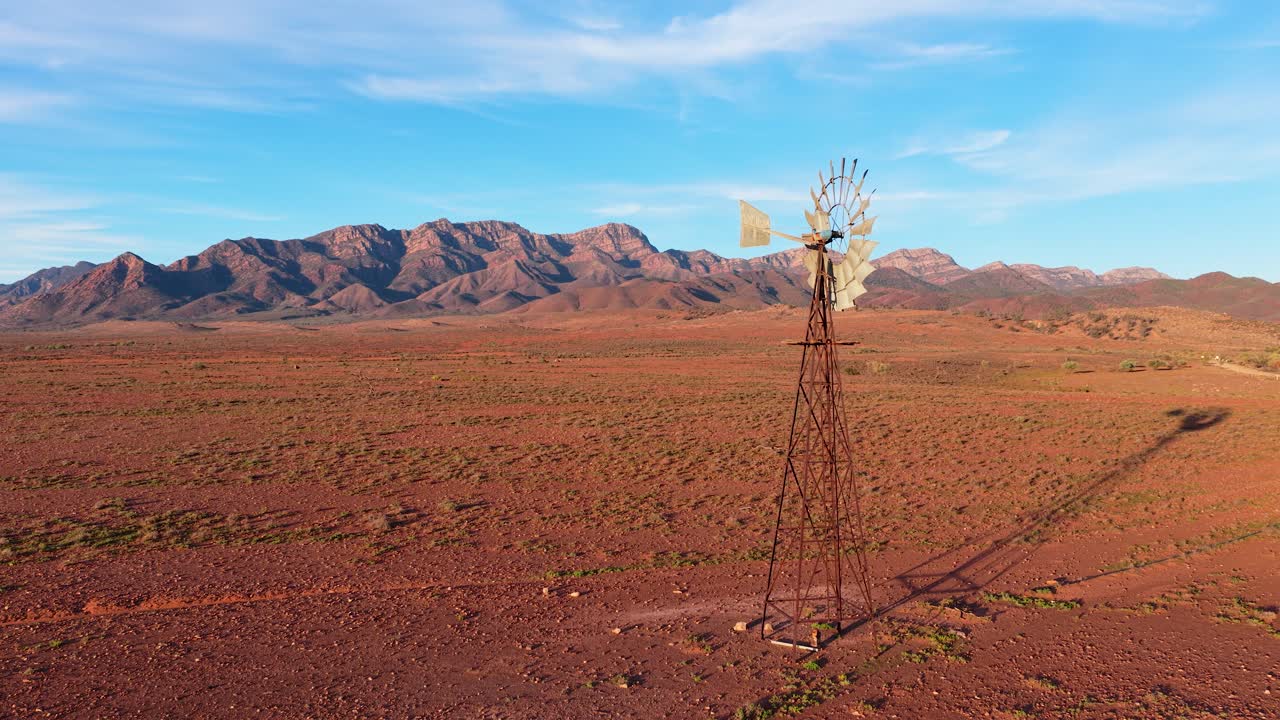 Slow smooth reverse shot of windmill, desert and Flinders Ranges mountains, South Australia