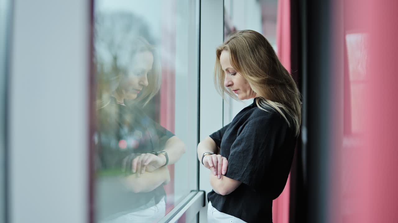 Anxious woman staring at watch near window - urban scene of silent waiting, Riga