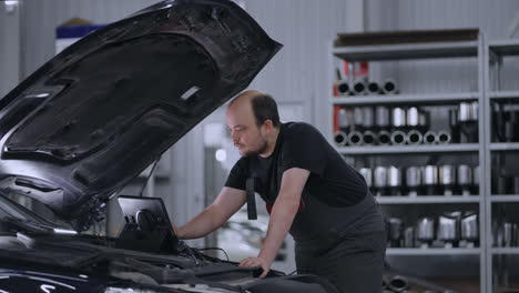 male mechanic uses a tablet computer with an augmented reality diagnostics software. specialist inspecting the car in order to find broken components inside the engine bay. modern car service.