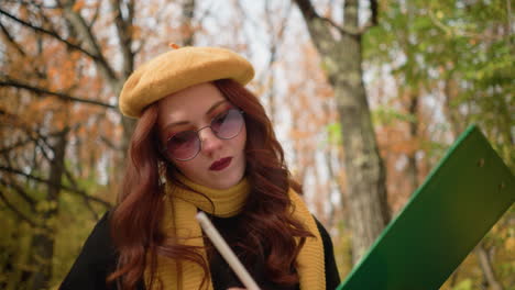 close up of hand of creative mind thoughtfully sketching on canvas, seated with head tilted, wearing stylish yellow beret and scarf, immersed in artistic expression amidst warm autumn scenery