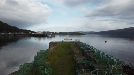 small boat float quietly on calm water near dock with distant hill under cloudy blue sky in scotland, peaceful scene reflect gentle wave and quiet mood of outdoor coast view in natural setting