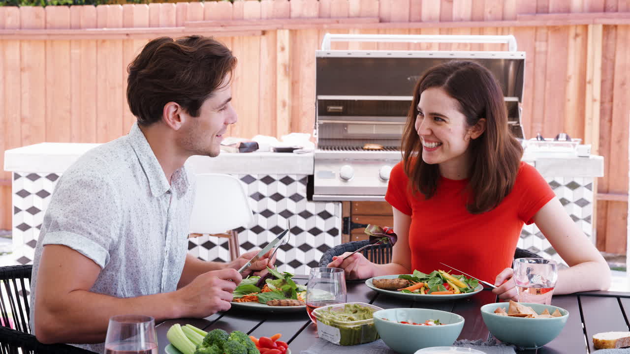 una pareja blanca comiendo almuerzo en una mesa en el jardín