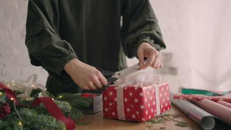 close-up: crop hands decorating wrapped box with string. female packing cardboard gift box on wooden table with various decorative items prepared for christmas celebration.