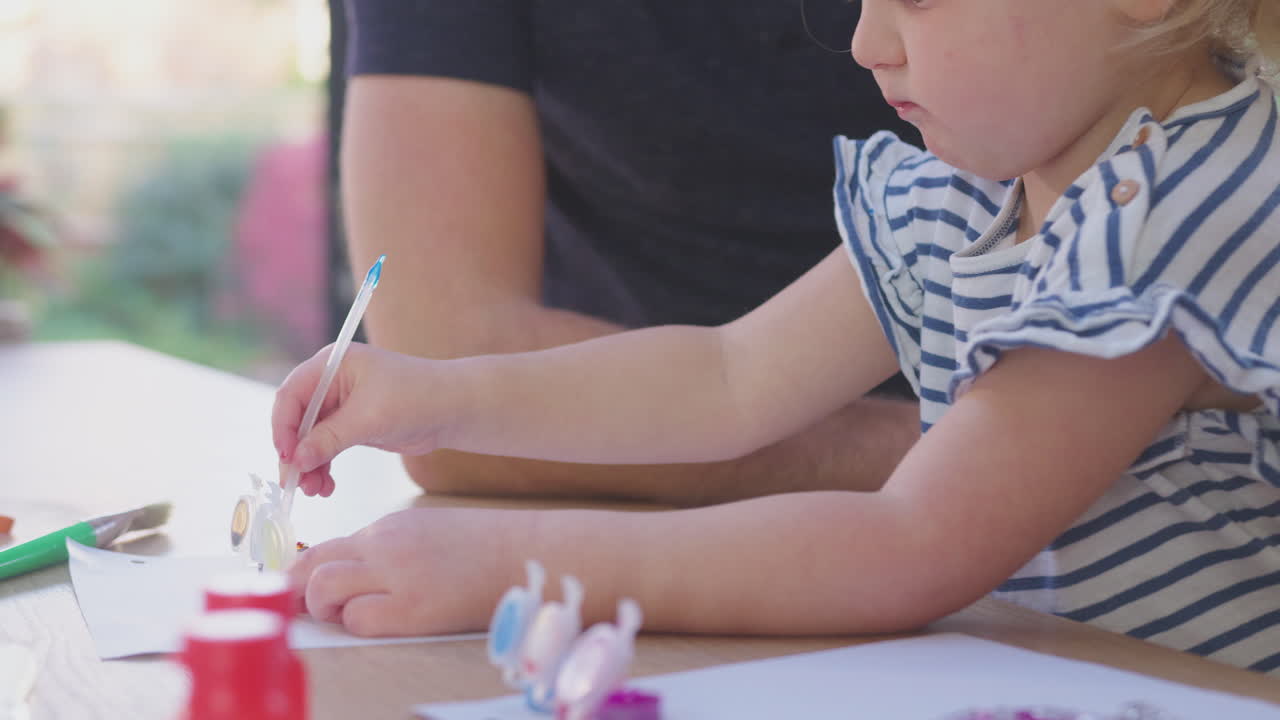 primer plano de padre e hija joven divirtiéndose en casa sentados a la mesa y pintando la decoración juntos - filmado en cámara lenta