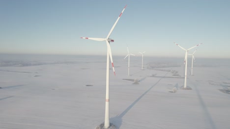 Toma-De-Drones-De-Turbinas-Eólicas-A-última-Hora-De-La-Tarde-En-Un-Paisaje-Plano-Y-Nevado-Del-Norte-De-Alemania