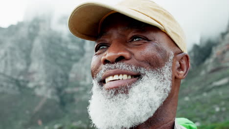 portrait of an elderly man with a white beard wearing a cap in the mountains