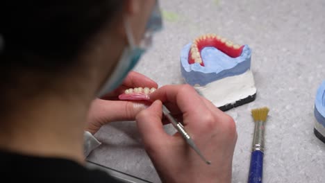 Making-of-dental-prosthetic-and-carving-out-dents-in-artificial-wax-gums-with-scalpel-at-the-workstation-by-healthcare-worker