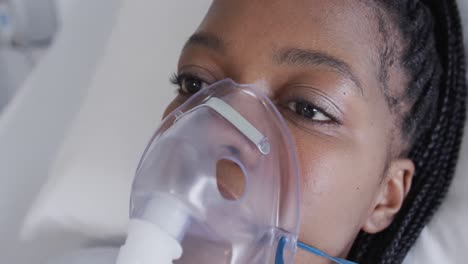 african american female patient with oxygen mask lying in bed in hospital room, slow motion