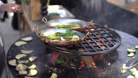 the cook roasts the courgettes. grilled vegetables. round bowl-shaped grill with a fire inside.