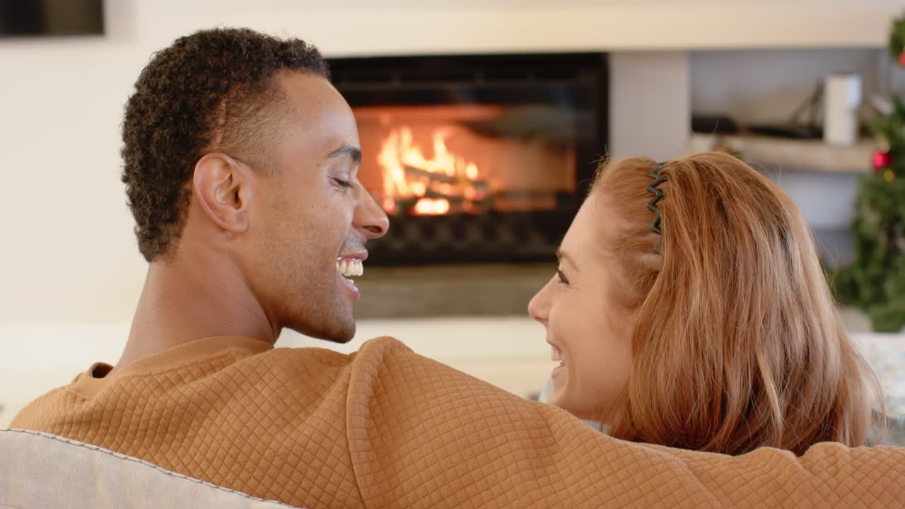 Diverse couple relaxing by cozy fireplace, enjoying warm holiday moments together