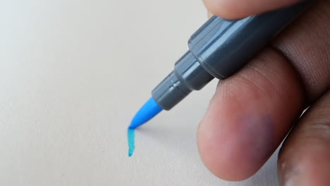 close up of a hand holding a blue marker and writing on paper